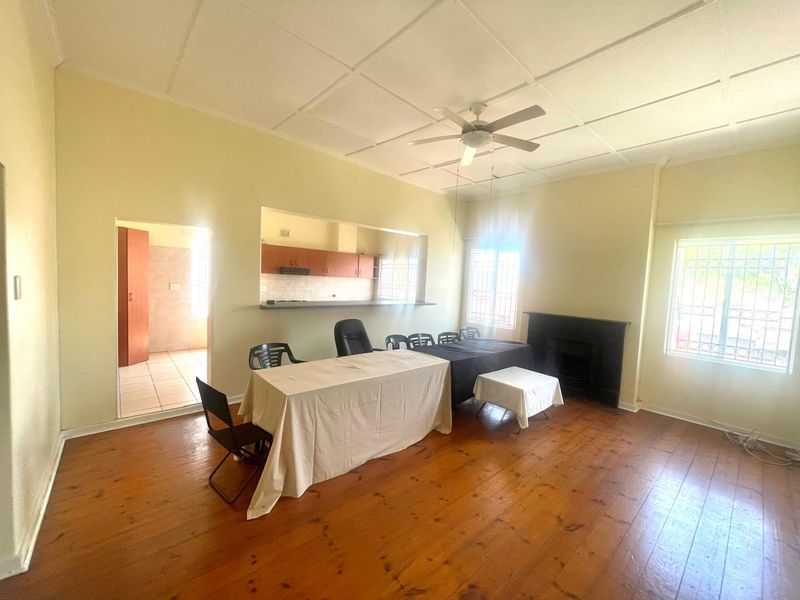 Open plan living and dining area featuring timber flooring, a ceiling fan, and a fireplace, with a convenient pass-through window to the kitchen.