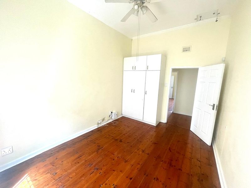 A vacant bedroom featuring polished timber flooring, built-in white cupboards, and a ceiling fan, offering a clean canvas for personalization.