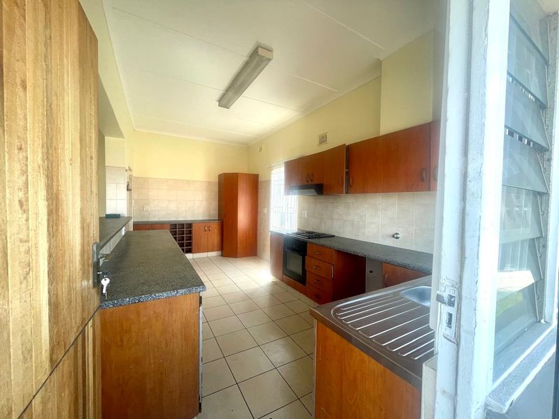 A functional kitchen featuring wooden cabinetry, laminate countertops, built-in oven, hob, and tiled flooring, offering a practical layout ready for modernization.