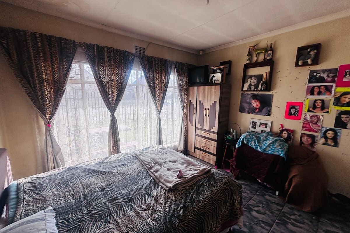 A bedroom featuring tiled flooring, large windows with security bars, and built-in cabinetry, offering a functional space with potential for cosmetic updates.
