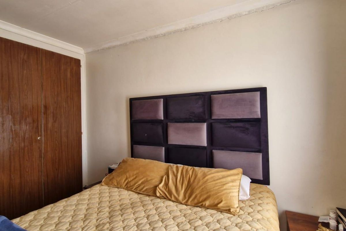 A bedroom featuring built-in wooden cupboards and a neutral wall finish, providing a functional sleeping space.