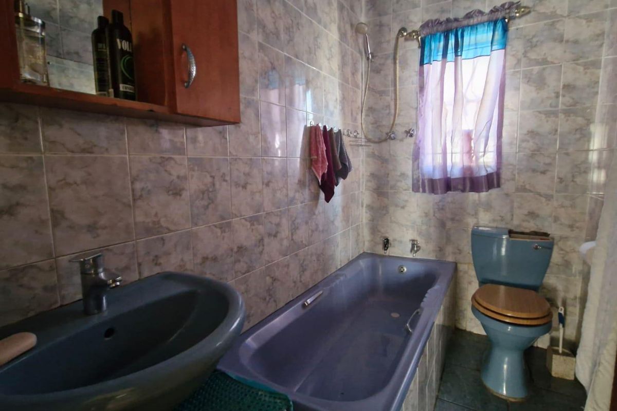 A dated bathroom featuring a blue suite, including a bathtub, pedestal basin, and toilet, with full-height wall tiling and a shower attachment.