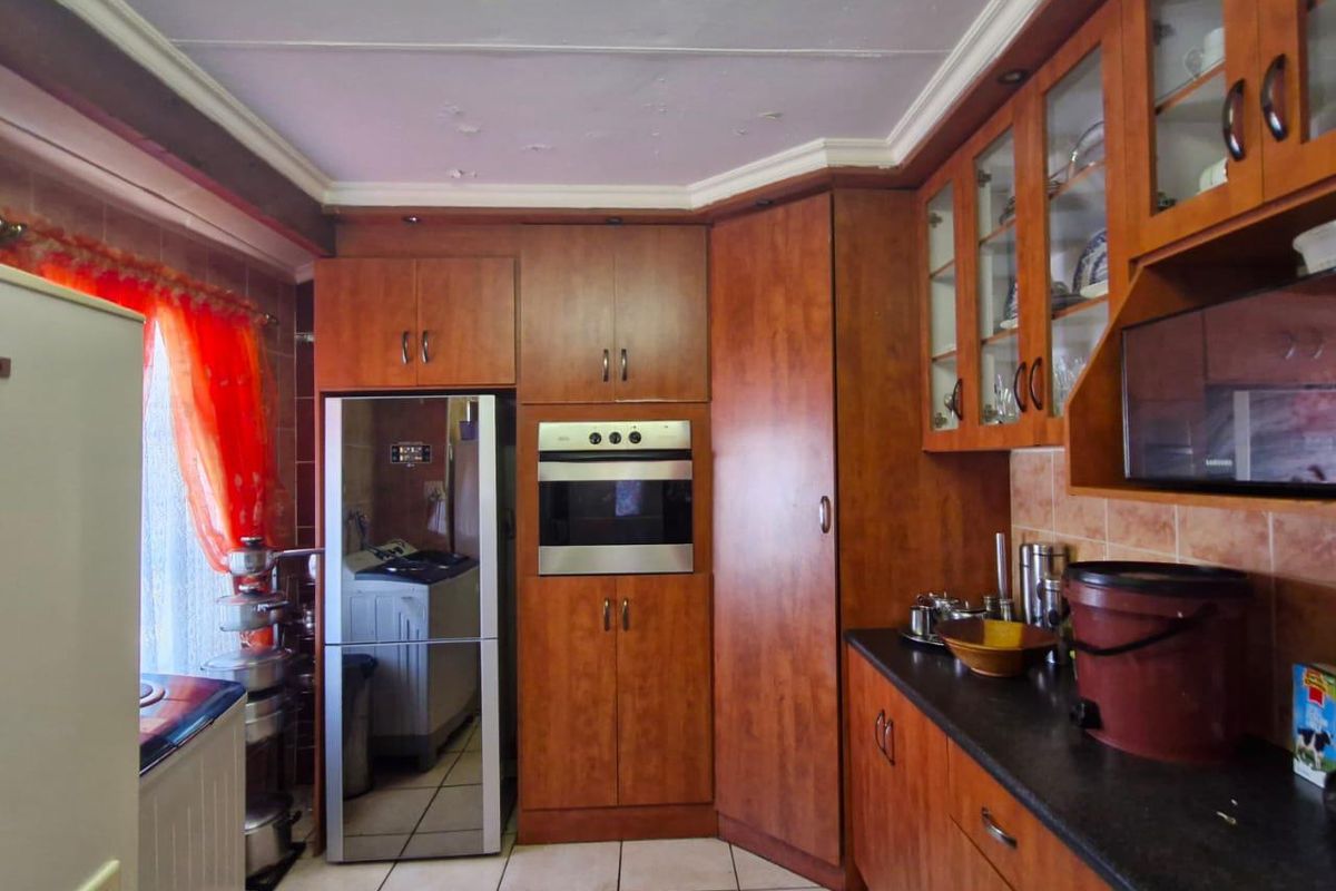 A functional kitchen featuring wood-finish cabinetry, dark countertops, built-in oven, and tiled flooring, offering a traditional layout with ample storage space.