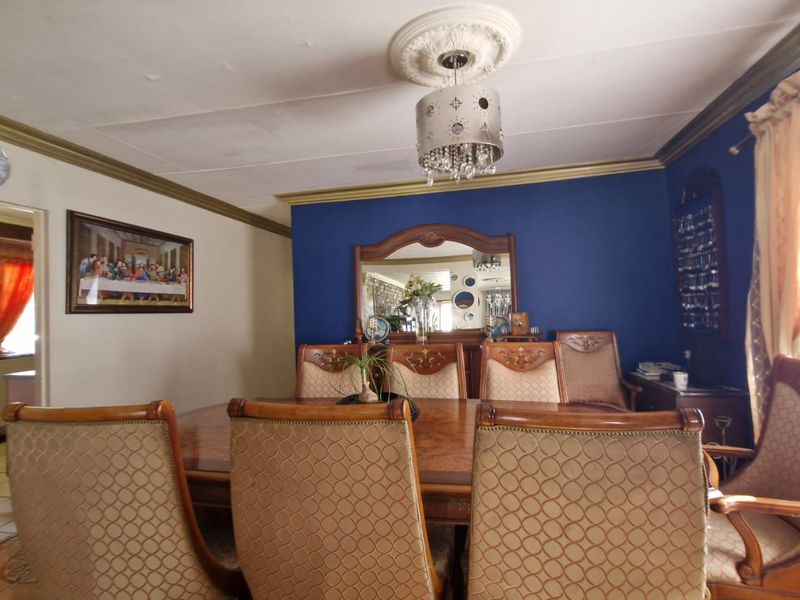 A formal dining room featuring a decorative ceiling rose, crown molding, and a bold blue accent wall.