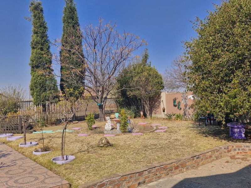 A spacious rear garden featuring a lawn area, established trees, and a brick retaining wall, providing a private outdoor space.