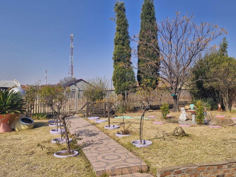 A landscaped garden featuring a paved walkway, mature trees, and a brick retaining wall, providing an open outdoor space.