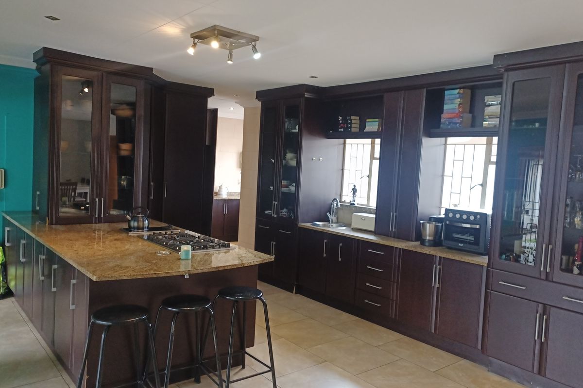 Spacious kitchen featuring dark wood cabinetry, granite countertops, a central island with a gas hob, and ample built-in storage with glass-fronted display units.