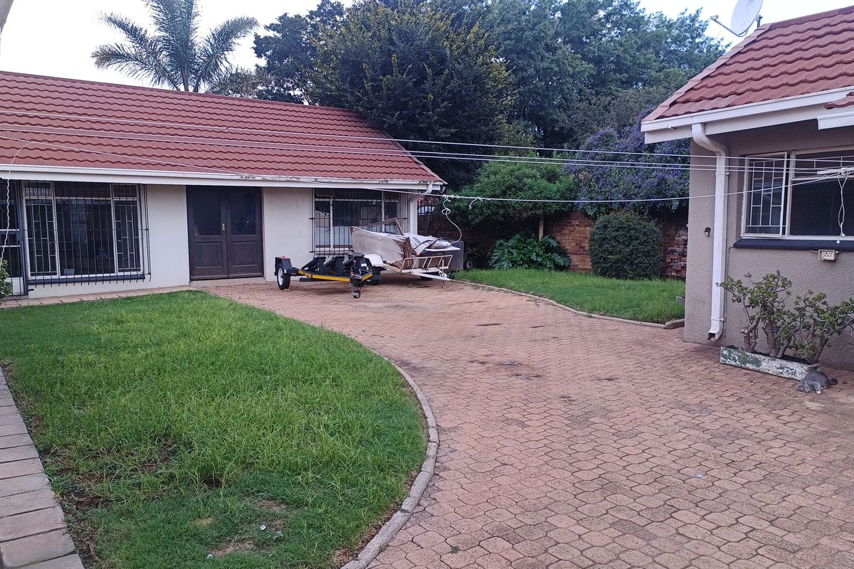 Rear exterior view of the property featuring a paved driveway, lawn area, and tiled roof structures with security bars on windows.