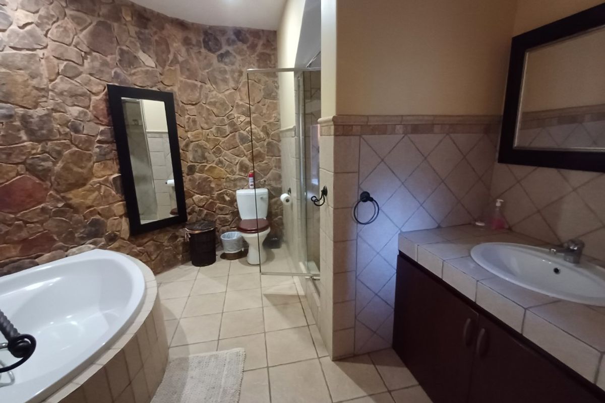 A spacious bathroom featuring a stone accent wall, a built-in bathtub, a tiled vanity with a drop-in basin, and a separate glass-enclosed shower.