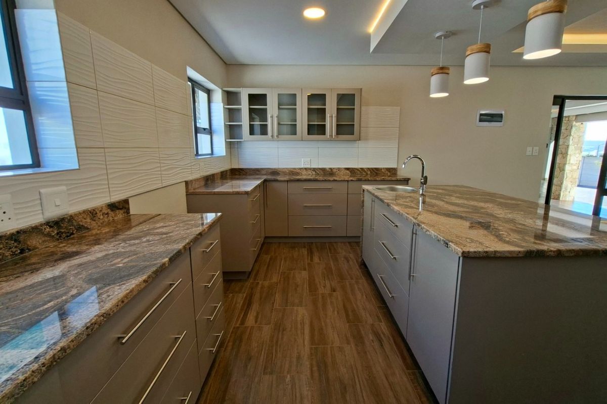 Modern kitchen featuring granite countertops, ample built-in cabinetry, a central island with a sink, and stylish pendant lighting.