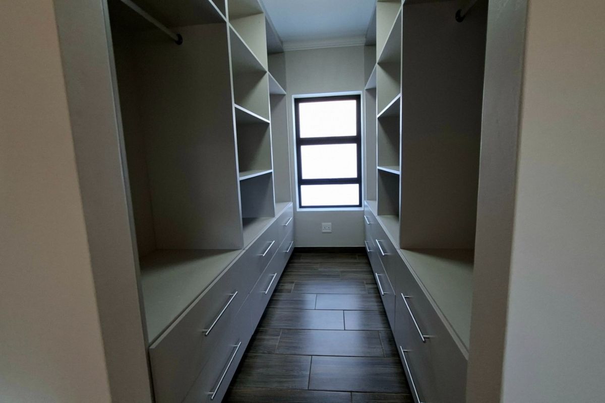A walk-in closet featuring extensive built-in cabinetry with ample shelving, hanging space, and drawers, finished with modern tiled flooring.