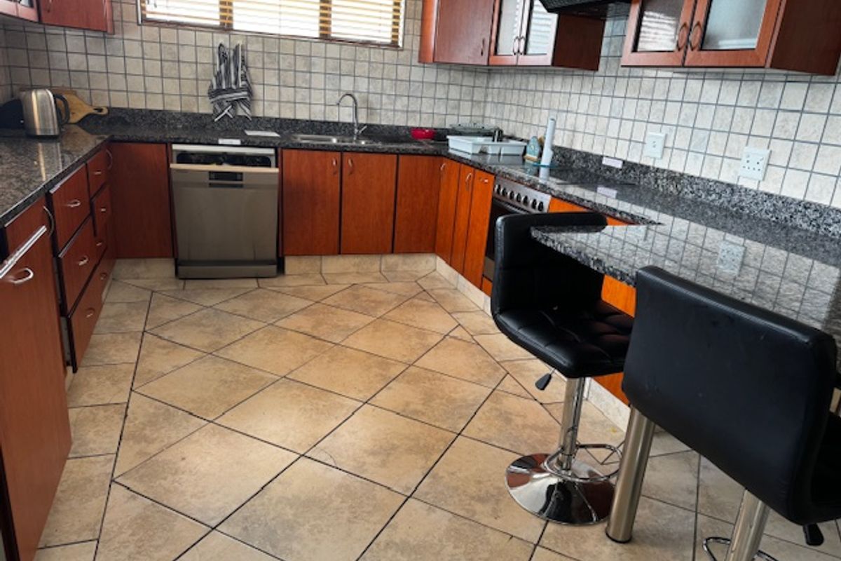 A functional kitchen featuring granite countertops, ample built-in cabinetry, a tiled backsplash, and a breakfast bar area with tiled flooring.