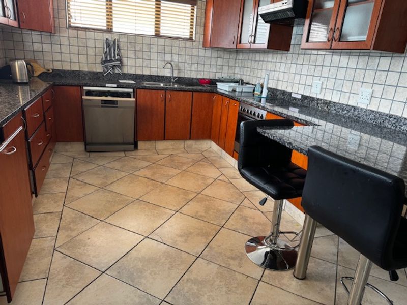 A functional kitchen featuring granite countertops, ample built-in cabinetry, a tiled backsplash, and a breakfast bar area with tiled flooring.