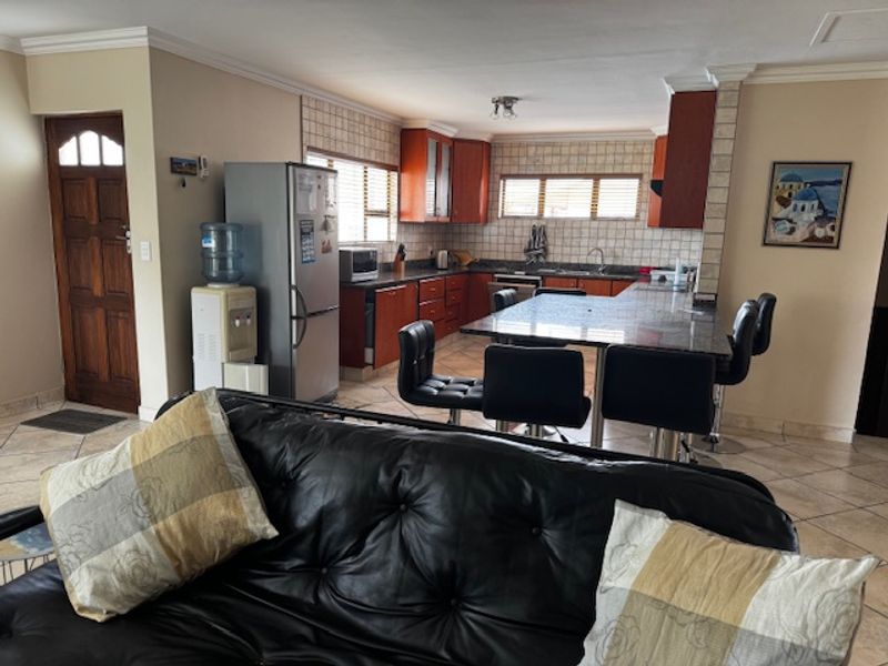 Open-plan living and kitchen area featuring dark wood cabinetry, granite countertops, a central kitchen island, and tiled flooring throughout.
