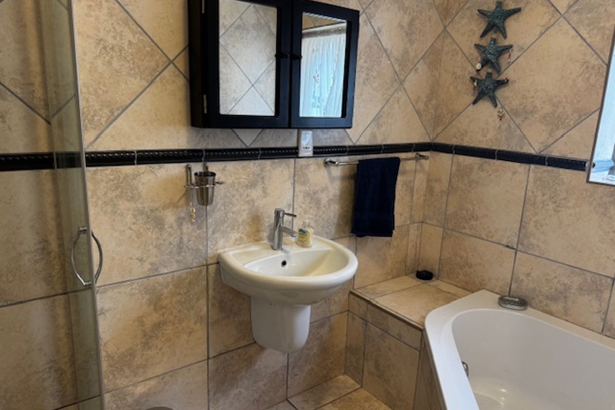 A functional bathroom featuring a wall-mounted basin, built-in bathtub, and a separate shower enclosure with neutral tiled finishes.