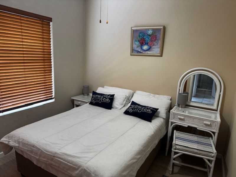 A cozy bedroom featuring neutral wall tones, wood-look flooring, and venetian blinds, providing a functional and comfortable sleeping space.