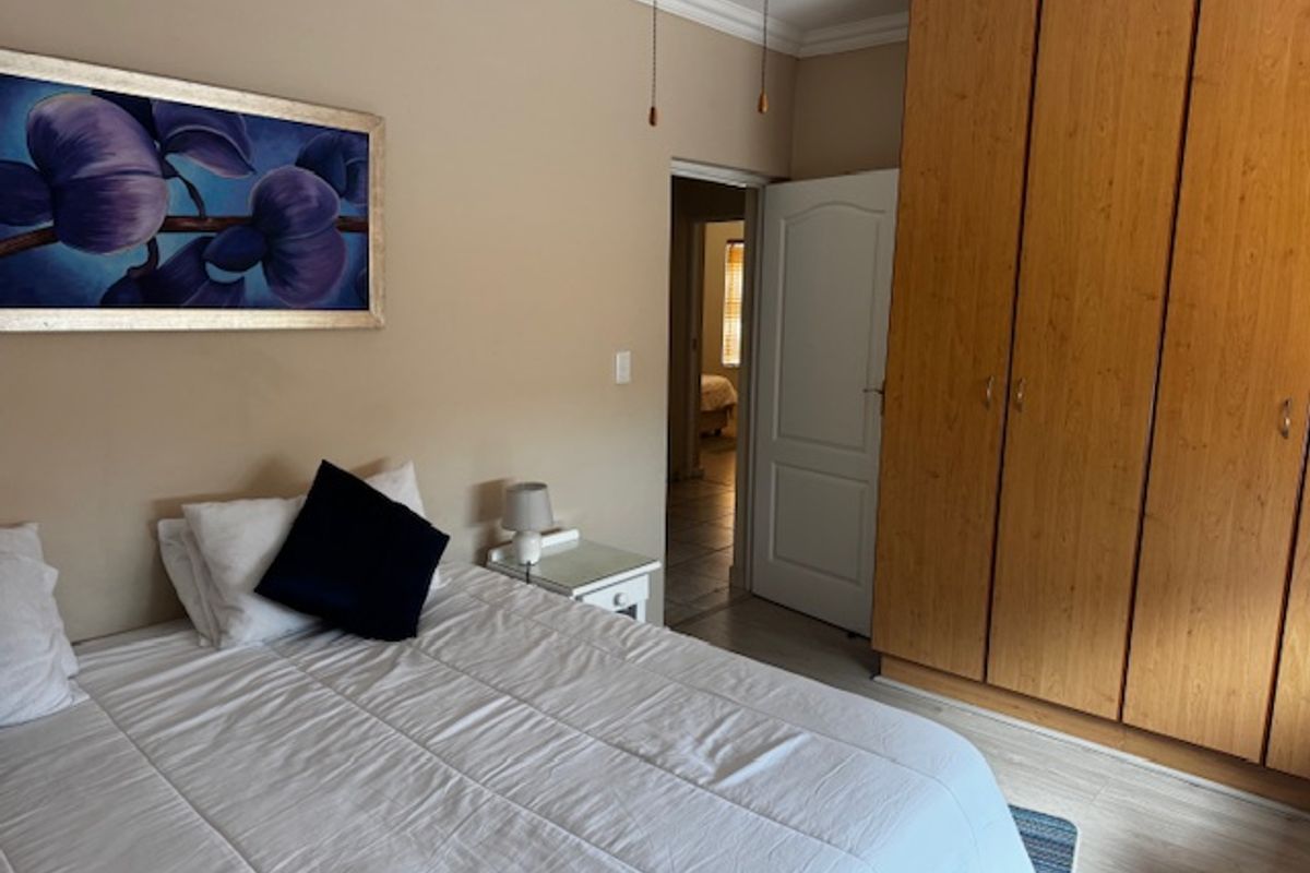 A bedroom featuring built-in wooden cupboards, laminate flooring, and decorative coving, providing a functional and neutral living space.