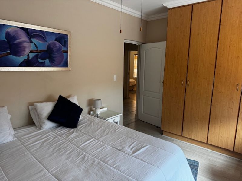A bedroom featuring built-in wooden cupboards, laminate flooring, and decorative coving, providing a functional and neutral living space.