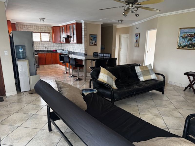 Open-plan living and kitchen area featuring tiled flooring, wooden cabinetry, granite countertops, and a ceiling fan.