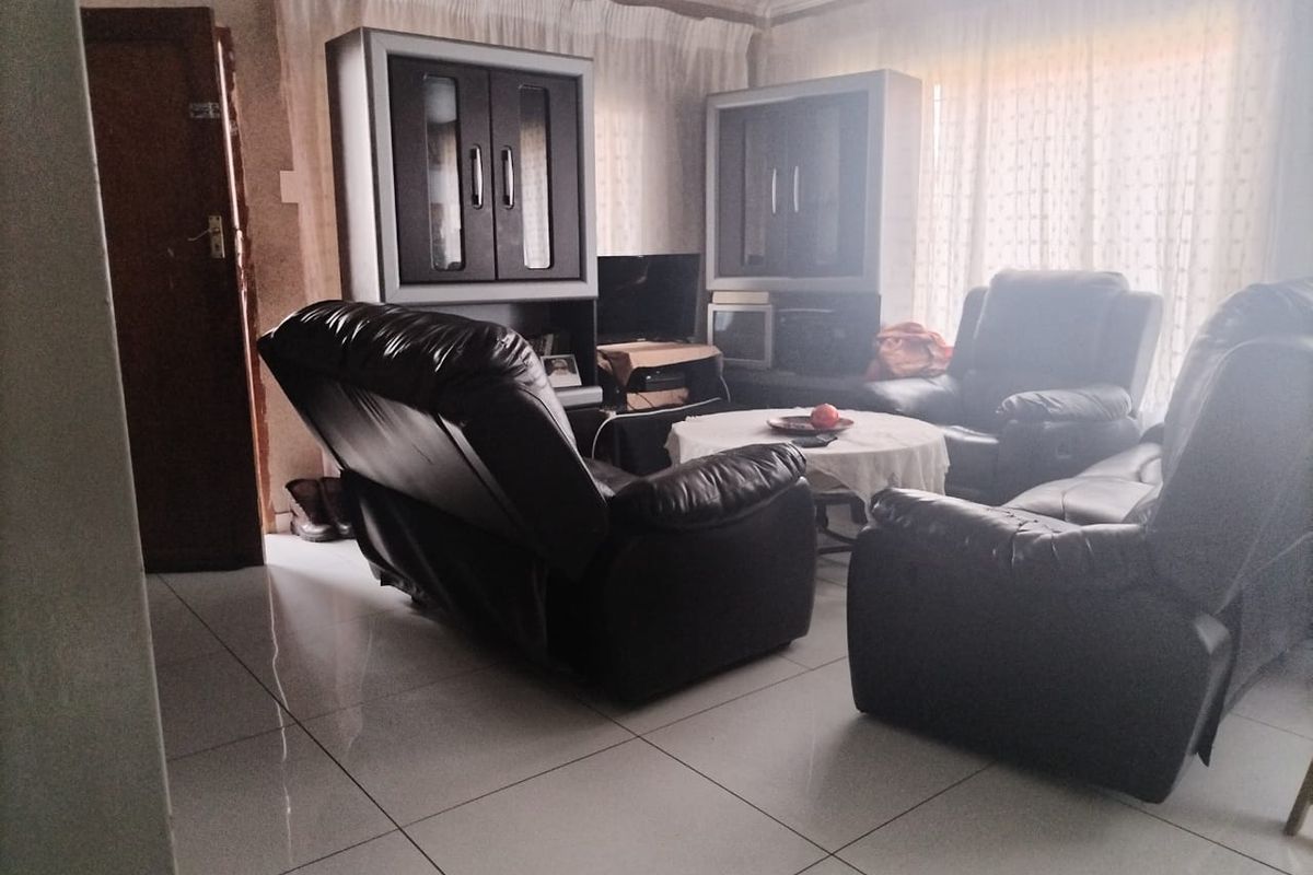 A living room featuring tiled flooring and decorative cornice, currently furnished with a seating arrangement.
