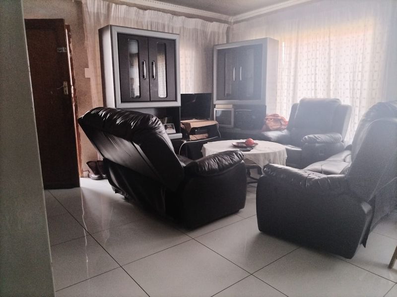 A living room featuring tiled flooring and decorative cornice, currently furnished with a seating arrangement.