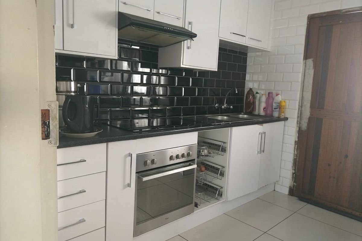 Modern kitchen featuring white cabinetry, black subway tile backsplash, built-in oven, electric hob, and integrated storage solutions.