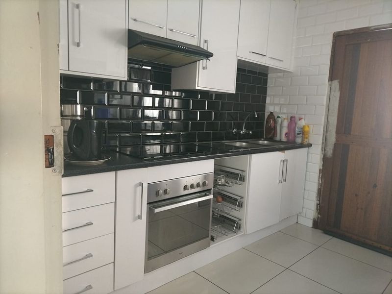 Modern kitchen featuring white cabinetry, black subway tile backsplash, built-in oven, electric hob, and integrated storage solutions.