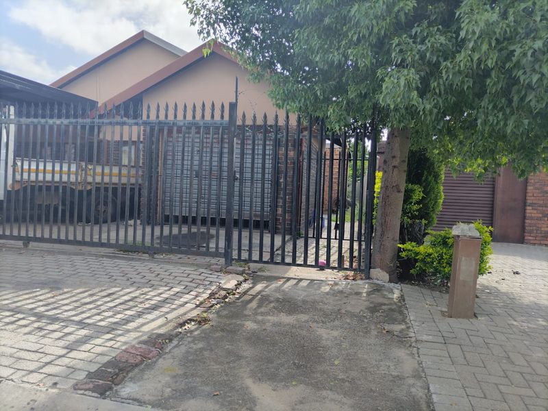 Front exterior view of the property featuring a metal security gate, brick facade, and paved driveway area.