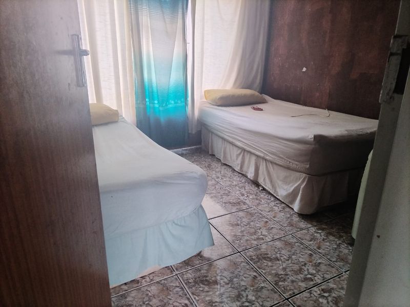 A bedroom featuring tiled flooring and window treatments, currently configured with two single beds.