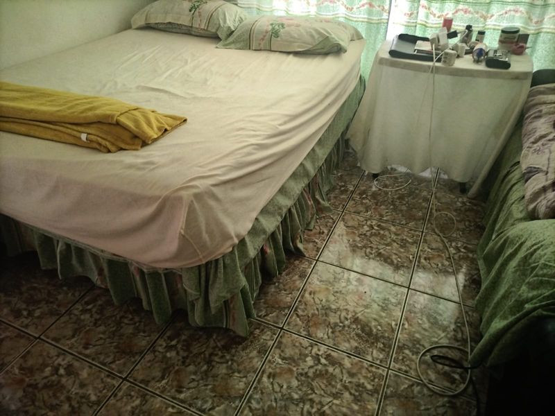 A bedroom featuring tiled flooring, currently furnished with a bed and side table.