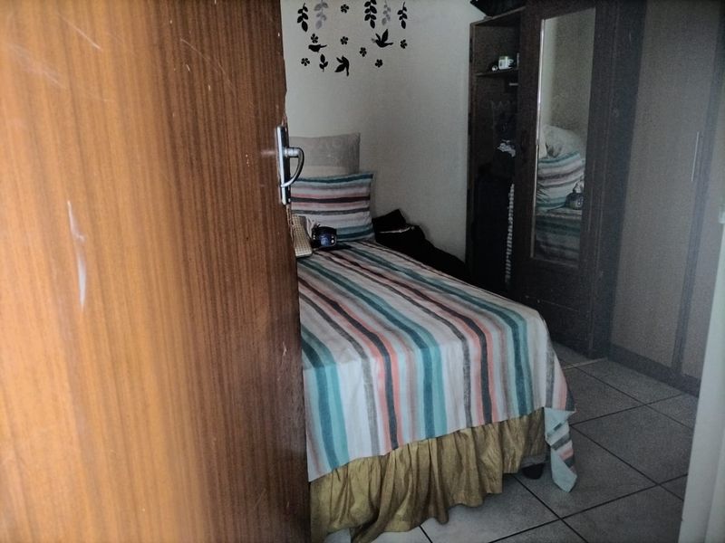 A compact bedroom featuring tiled flooring and a built-in wardrobe, viewed through a partially open wooden door.