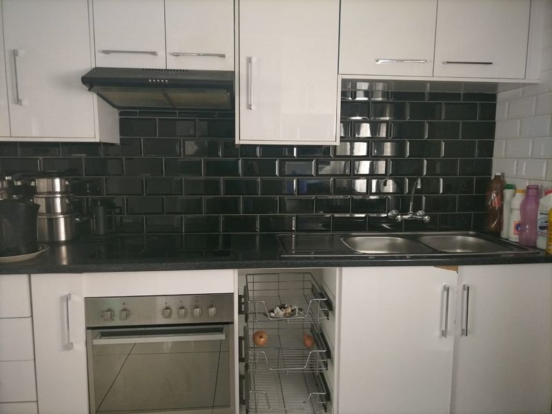 A functional kitchen featuring white cabinetry, black subway tile backsplash, integrated oven, hob, and a double bowl sink with drainer.