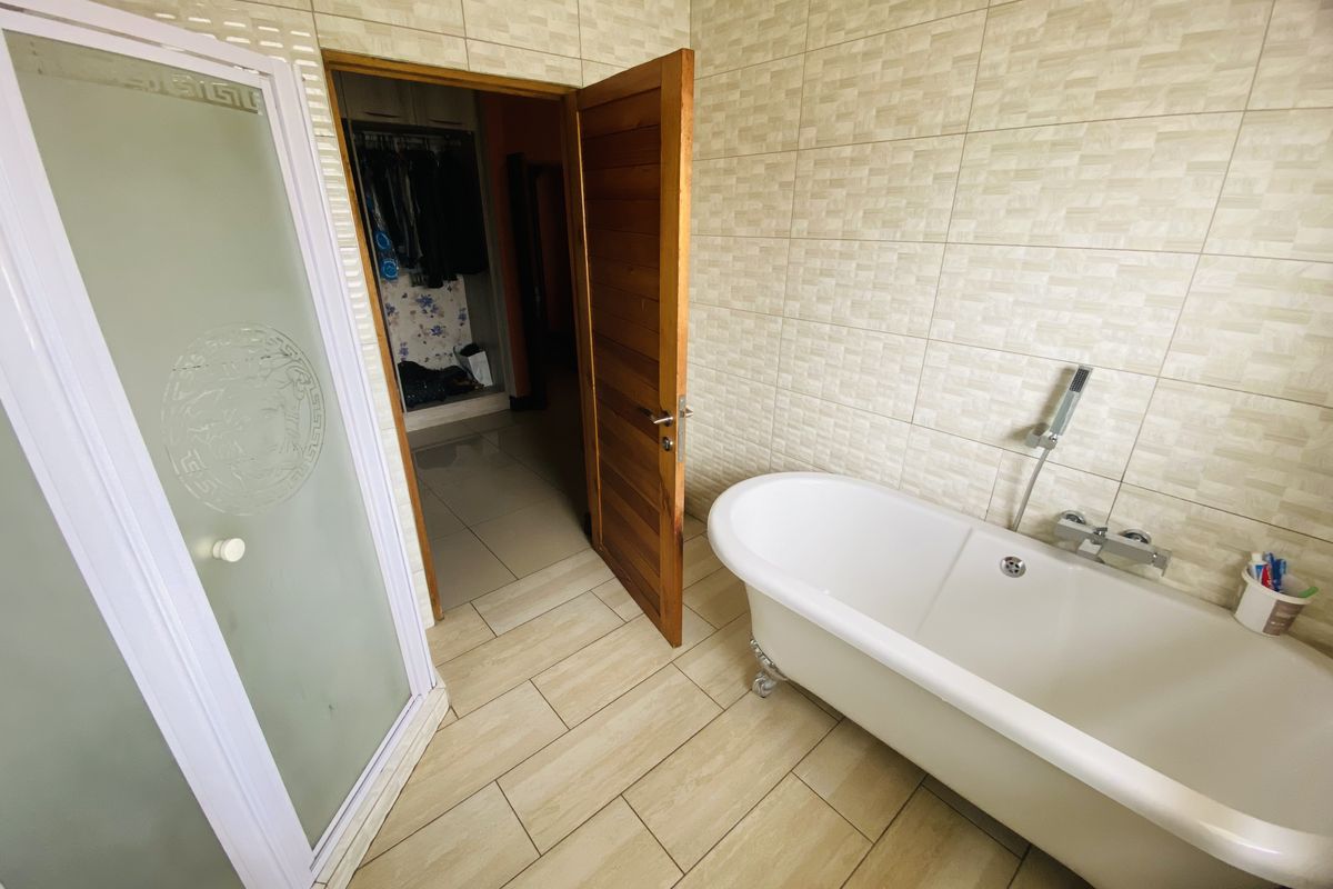 A functional bathroom featuring a classic freestanding bathtub, a separate shower enclosure, and neutral ceramic tiling throughout.