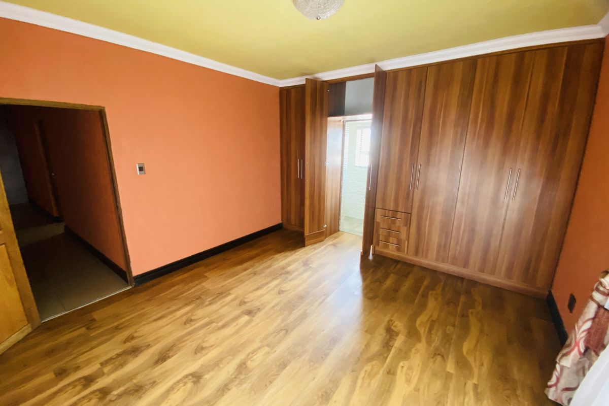 A spacious bedroom featuring built-in wooden wardrobes, laminate flooring, and a bright orange wall finish with a contrasting yellow ceiling.