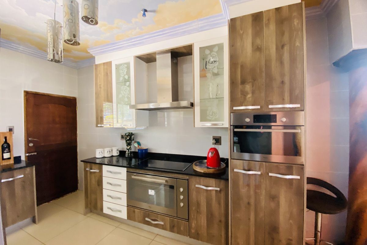 A functional kitchen featuring wood-finish cabinetry, stone countertops, integrated oven and hob, and a unique decorative ceiling finish.