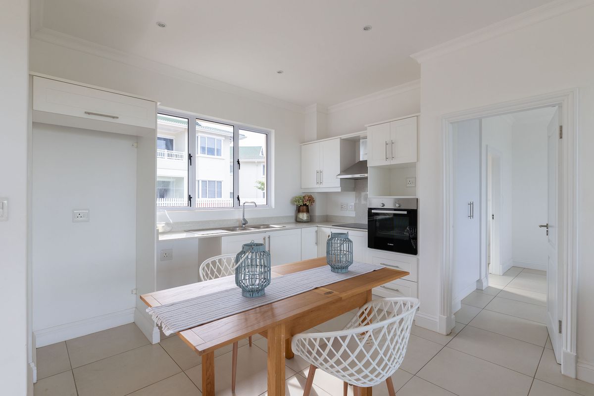 A bright, modern kitchen featuring white cabinetry, built-in oven, extractor fan, and tiled flooring, with an integrated layout and ample natural light.