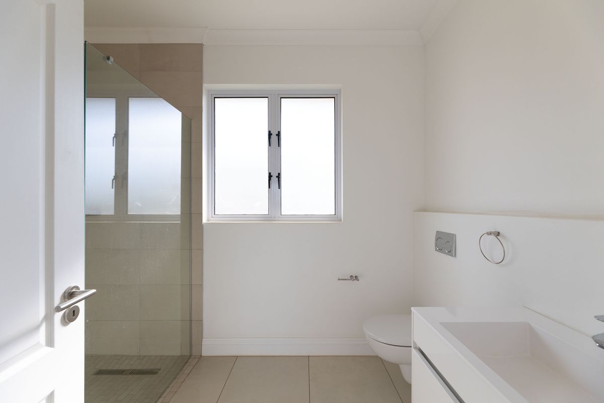 A clean, modern bathroom featuring a glass-enclosed shower, wall-mounted toilet, and a sleek built-in vanity with neutral tiling.