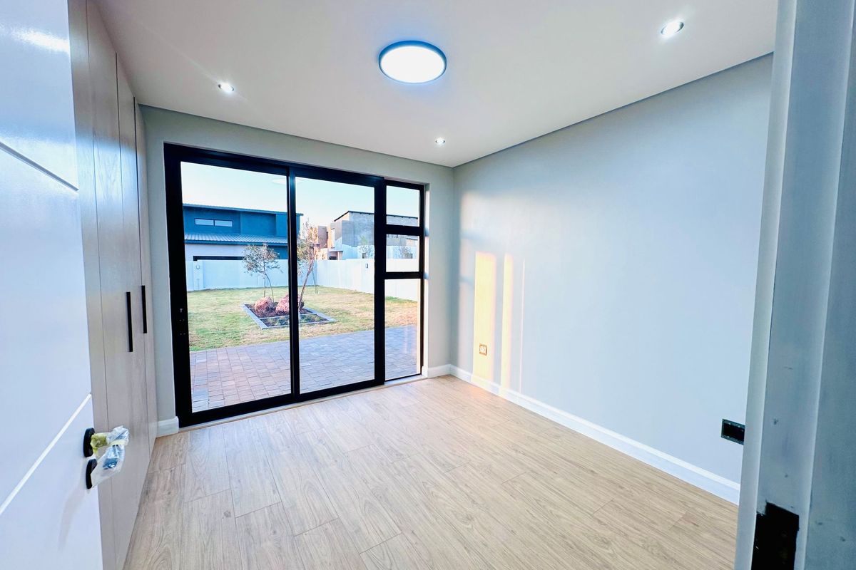 A bright, modern bedroom featuring light wood-look flooring, built-in cabinetry, and large sliding glass doors providing direct access to the rear garden.