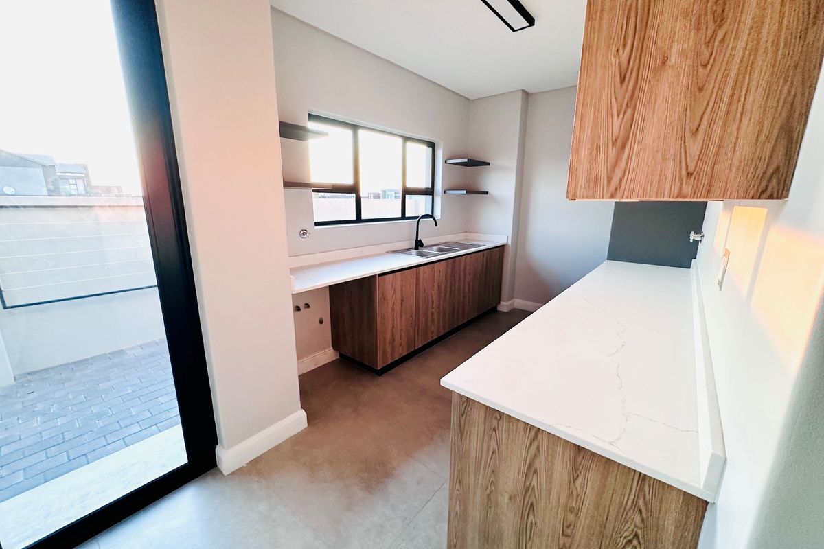 Modern kitchen featuring wood-grain cabinetry, stone countertops, a double sink, and direct access to an outdoor patio area.