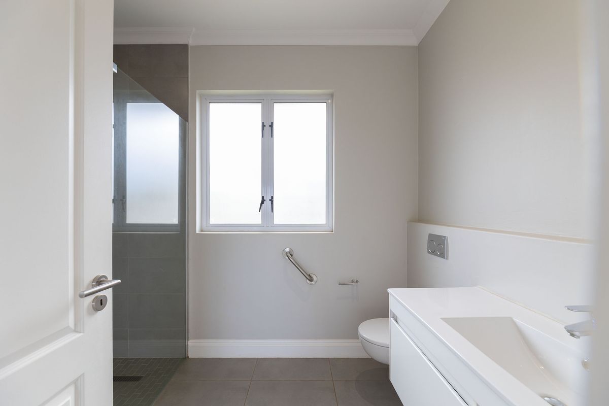Modern bathroom featuring a wall-mounted vanity, walk-in shower with glass screen, and accessible grab rail.