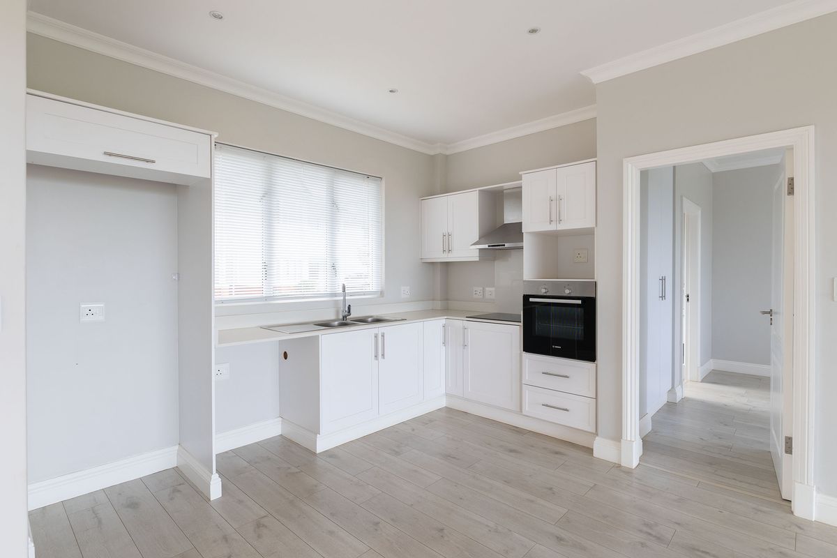 A modern, clean kitchen featuring white cabinetry, integrated oven, hob, extractor fan, and light wood-look flooring in an open-plan layout.