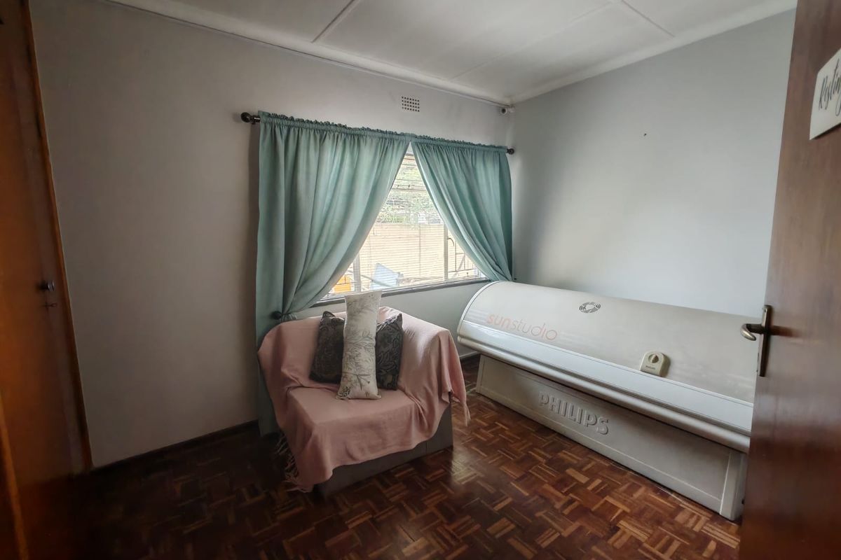 A bedroom featuring parquet flooring and a window with security bars, currently utilized as a tanning studio.