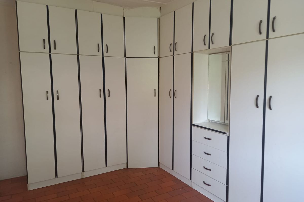 A bedroom featuring extensive built-in white cabinetry with integrated drawers and a vanity mirror, set against terracotta tiled flooring.