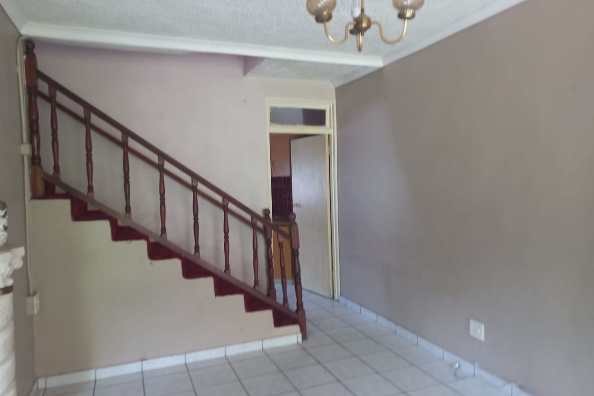 An open living area featuring a traditional wooden staircase with carpeted treads, tiled flooring, and a central ceiling light fixture.