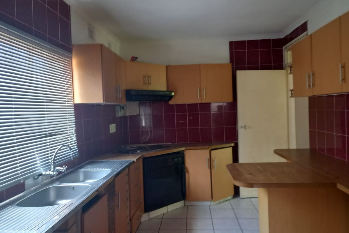 A dated kitchen featuring wooden cabinetry, dark tiled splashbacks, a double sink, and built-in oven with extractor fan.