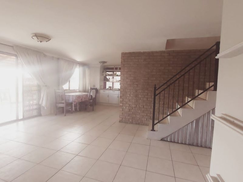 Open plan living area featuring tiled floors, an exposed brick feature wall, and a staircase with metal railing leading to the upper level.