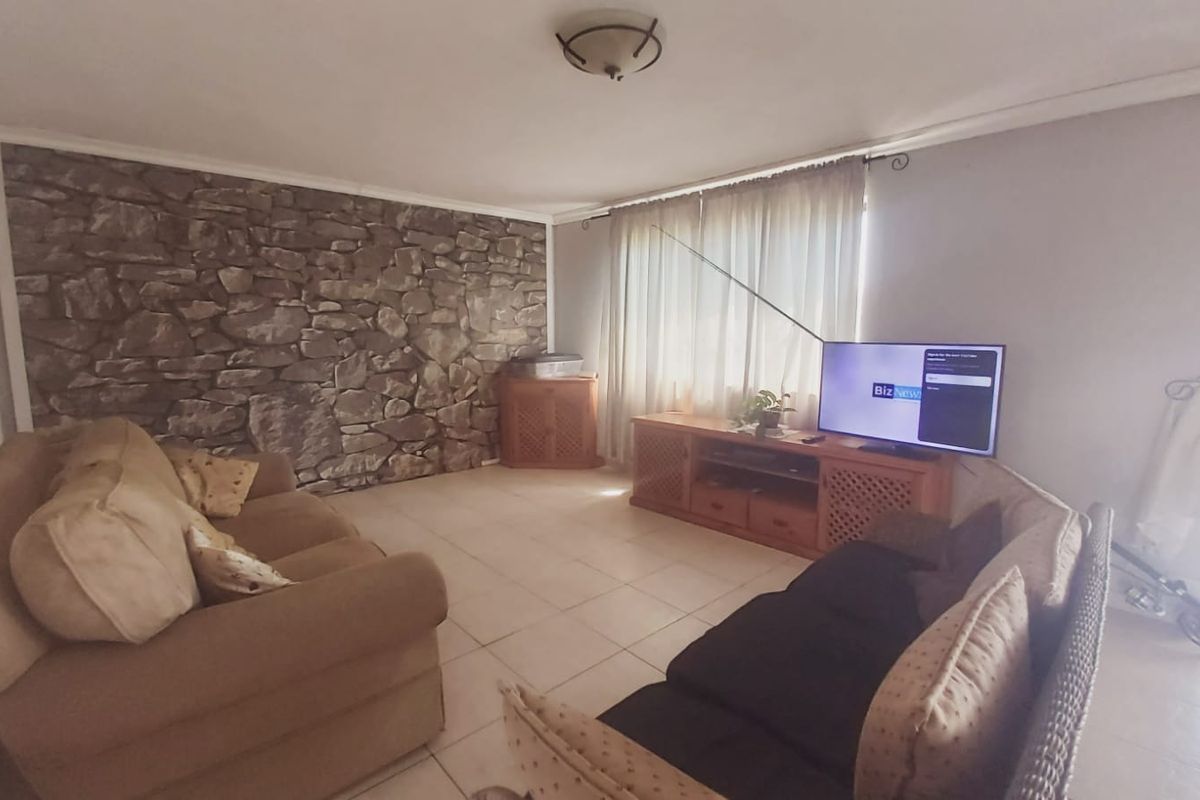 A living room featuring a stone accent wall, tiled flooring, and natural light through large windows.