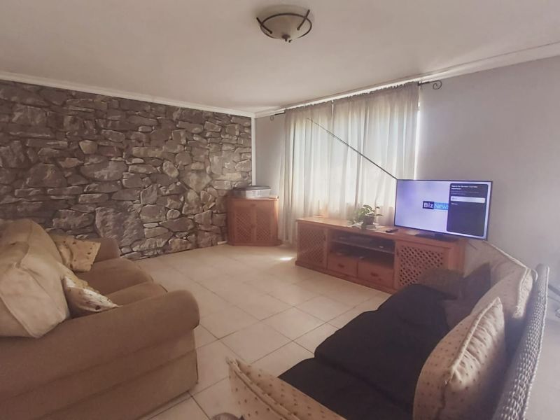 A living room featuring a stone accent wall, tiled flooring, and natural light through large windows.