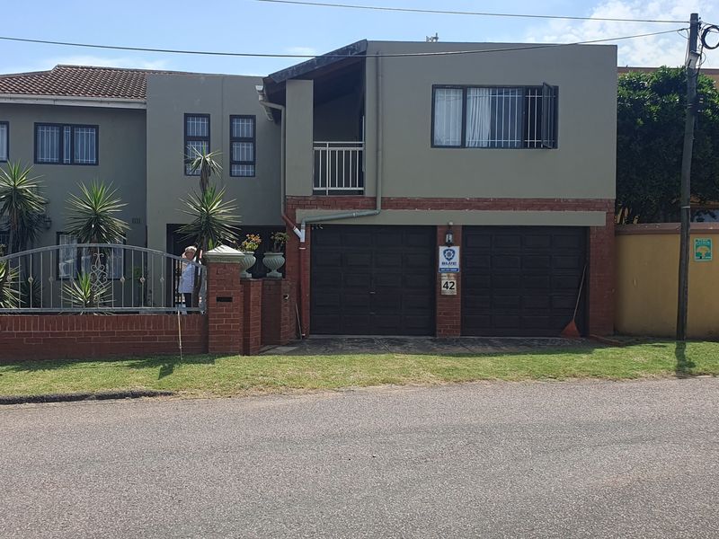 Front elevation of a two-story residential house featuring a double garage, balcony, and secure brick and metal perimeter fencing.