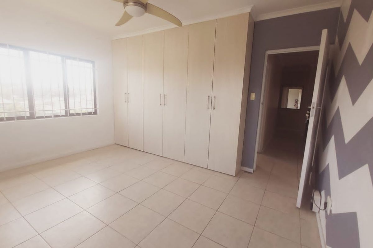 A bright, empty bedroom featuring built-in cupboards, tiled flooring, and a ceiling fan, offering a clean canvas for personalization.